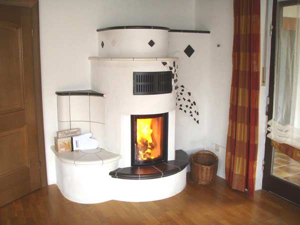 Runder Kachelofen mit Rautenmotiven, Ofenbank und Feuer im Sichtfenster