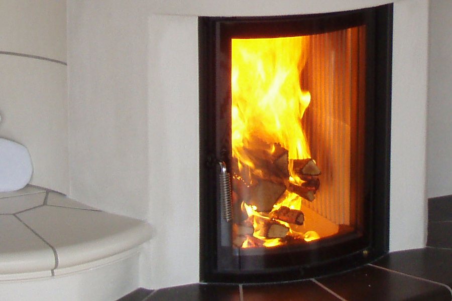 Brennendes Holzfeuer hinter der gewölbten Scheibe eines Kachelofens